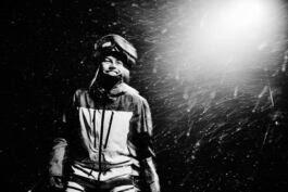 Hedvig Wessel Free ski World Chamption in a ski suit stands in the snow at night, illuminated by bright light. Snowflakes swirl around them in motion. 